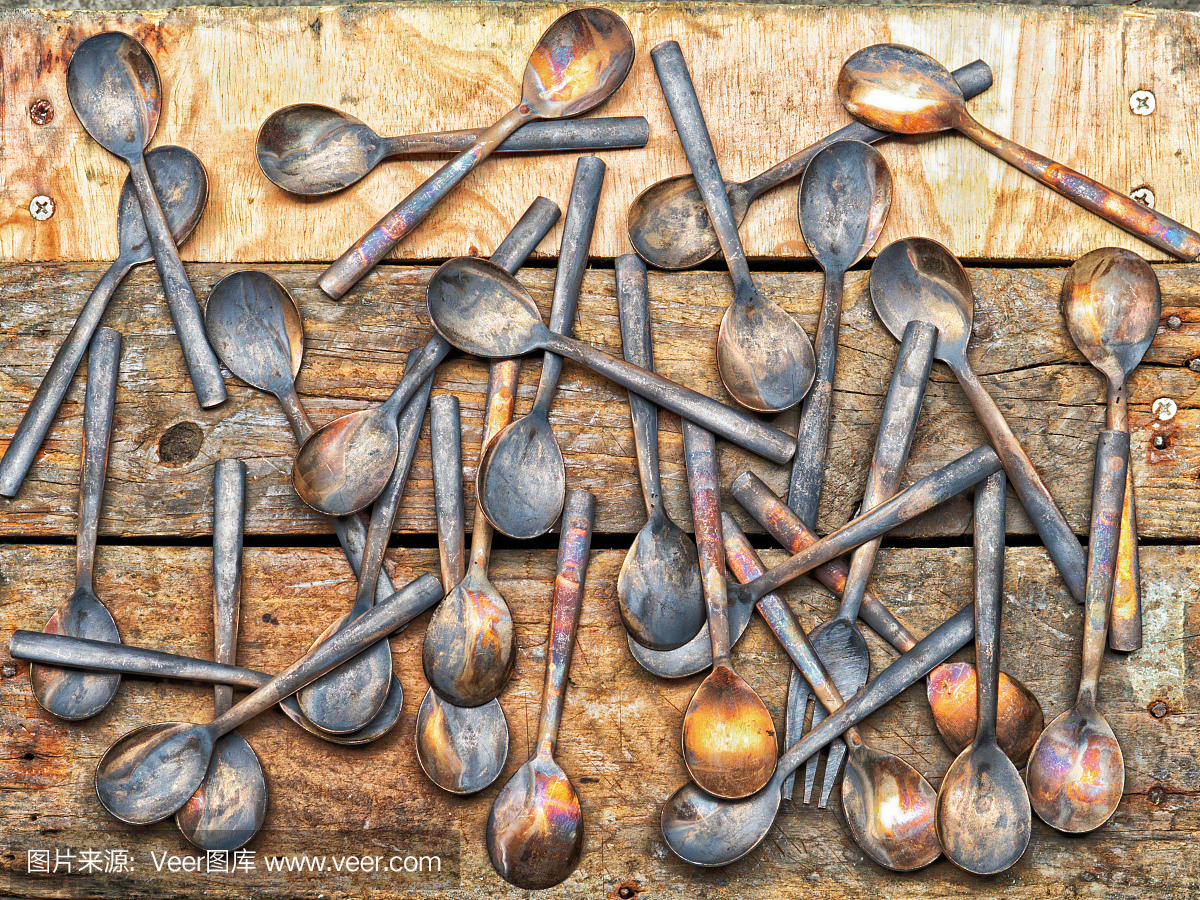 工作过程中手工青铜餐具的勺子和叉子在木制背景,老式工业背景